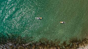 An aerial view of a beach with two boats and rocky shoreline.