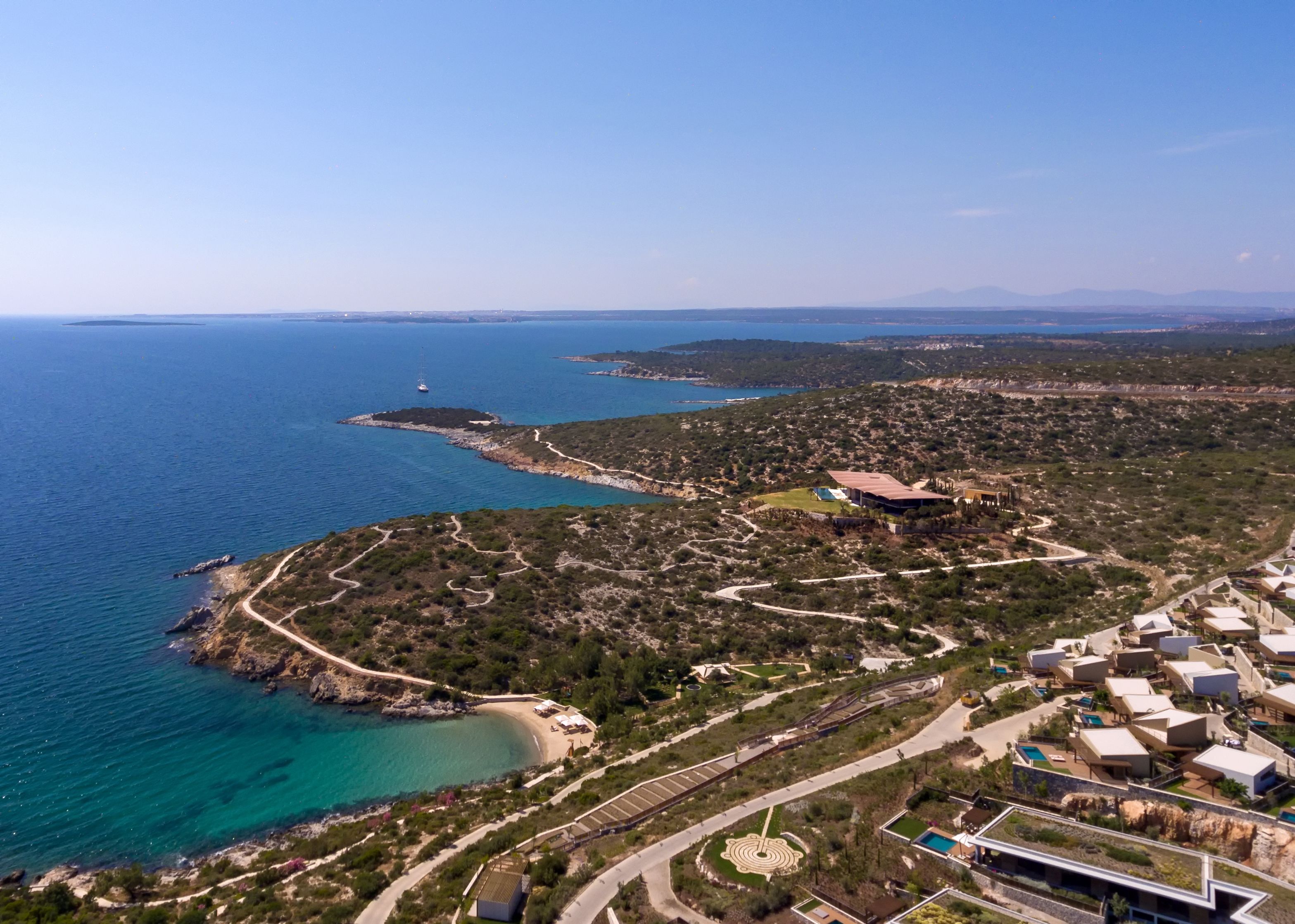 An aerial view of a coastal area with a beach, a marina, and a resort complex with modern architecture.
