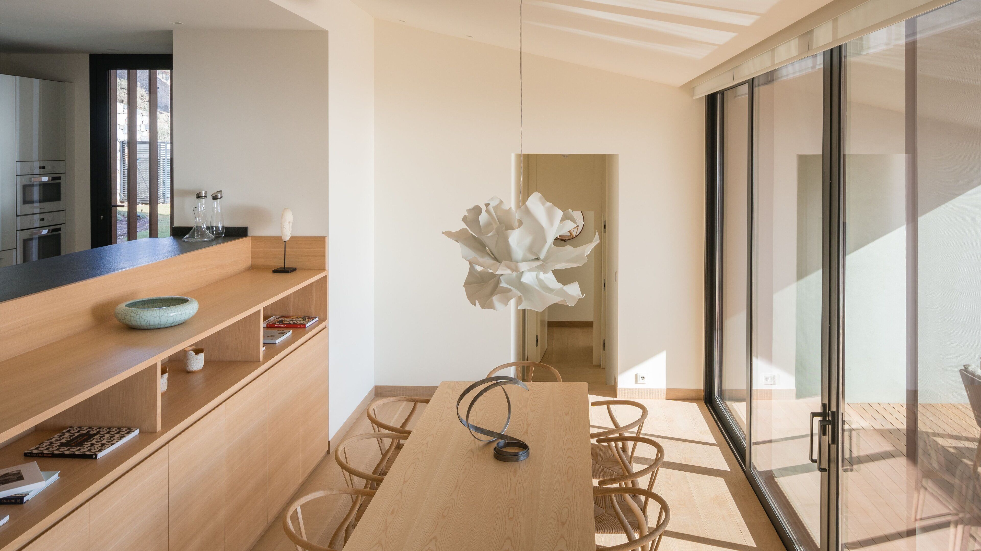 Una cocina moderna con armarios de madera, encimera negra y vistas al exterior a través de un amplio ventanal.