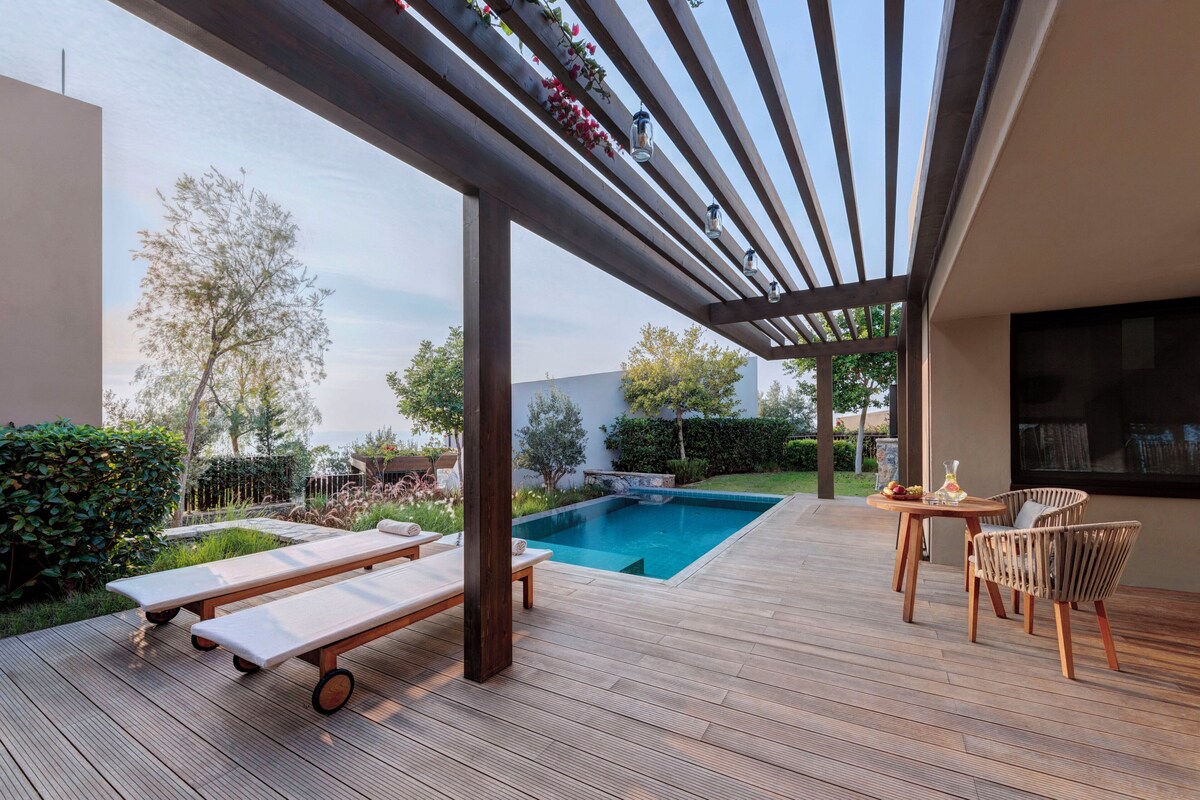 Una terraza de madera con piscina, sillas de descanso y una mesa con sillas.
