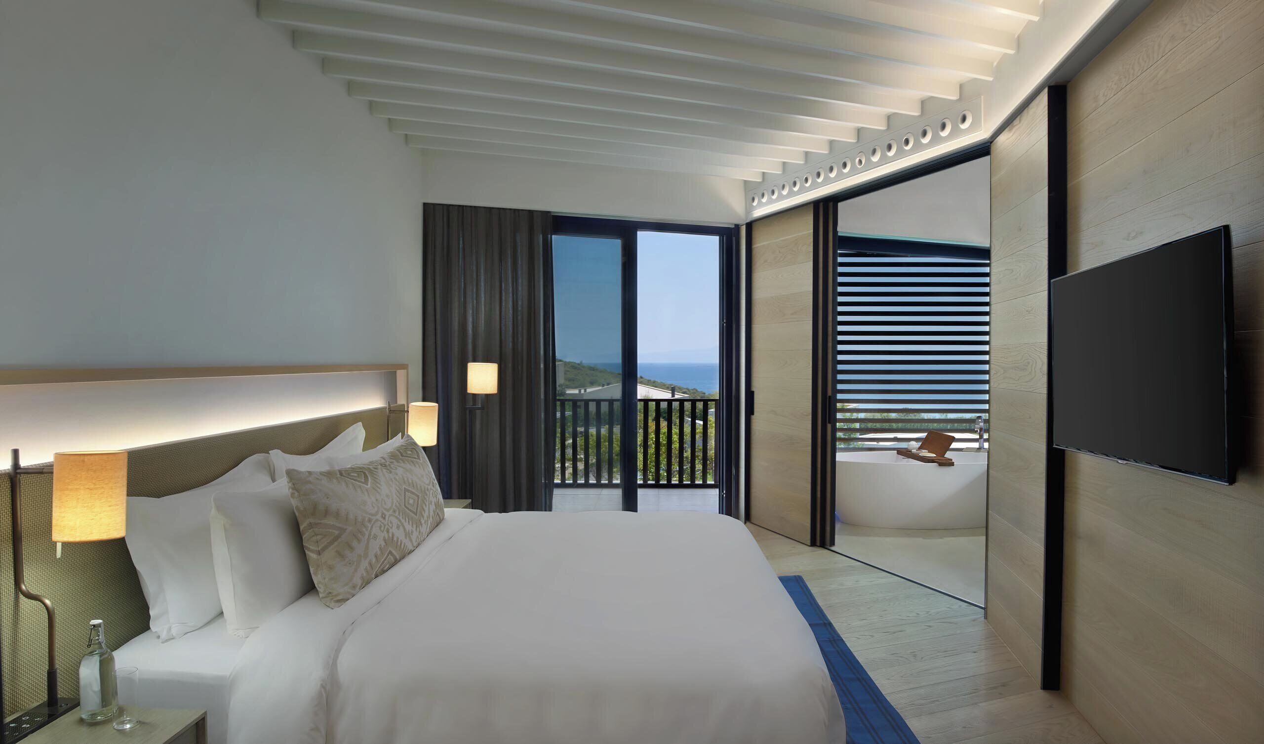 A modern hotel room with a large bed, a flat-screen TV, a balcony with a view, and a sliding door.