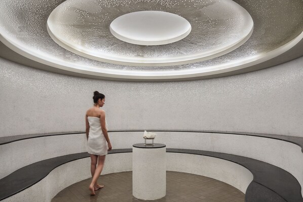 A woman in a white dress standing in a modern, circular room with a central column and a ceiling with concentric circles. - Six Senses Kaplankaya (Milas)