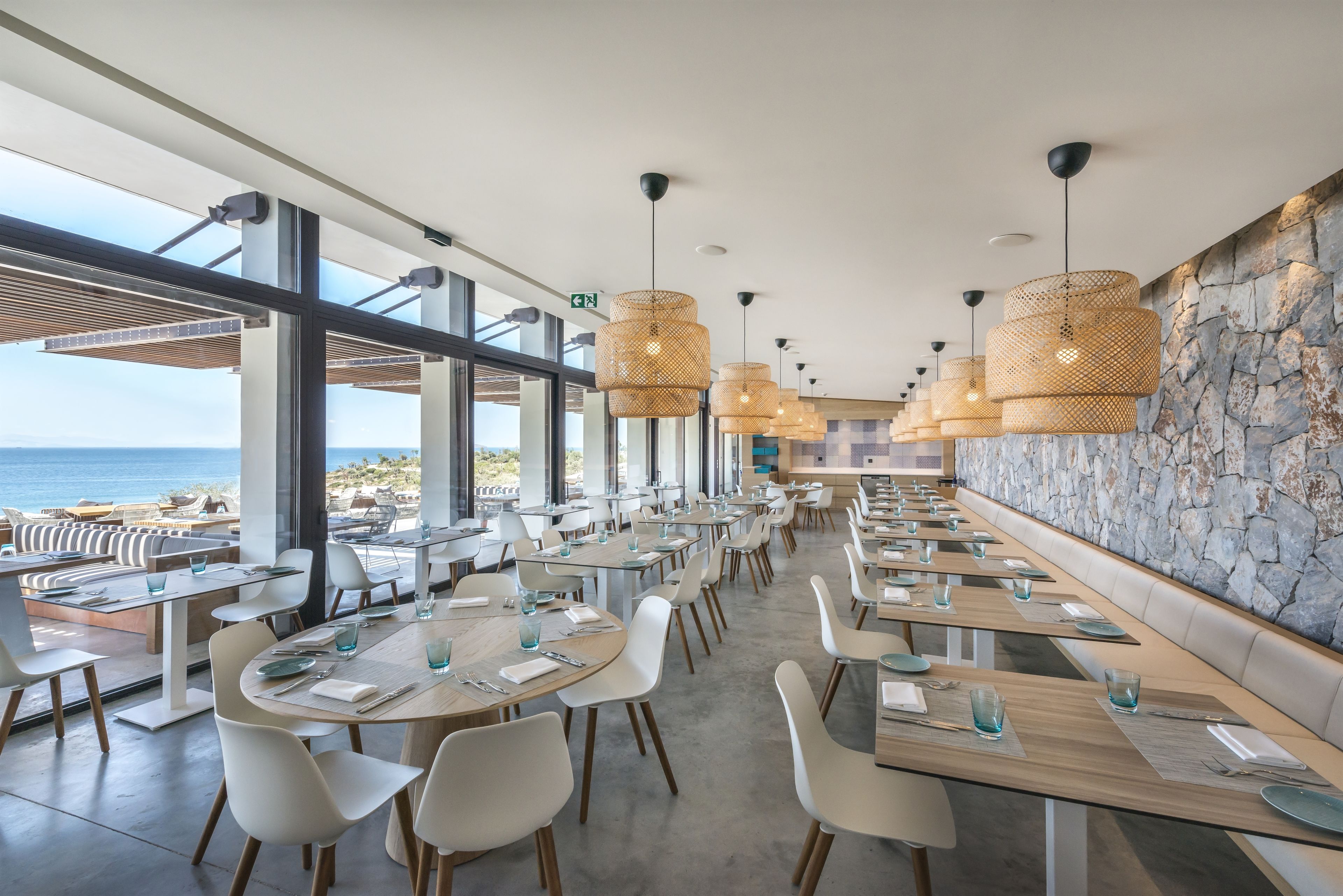 Un restaurante moderno con mesas largas, sillas blancas y lámparas de mimbre colgantes.