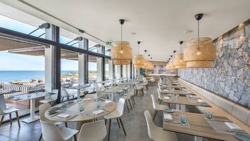 Un restaurante moderno con mesas largas, sillas blancas y lámparas de mimbre colgantes.