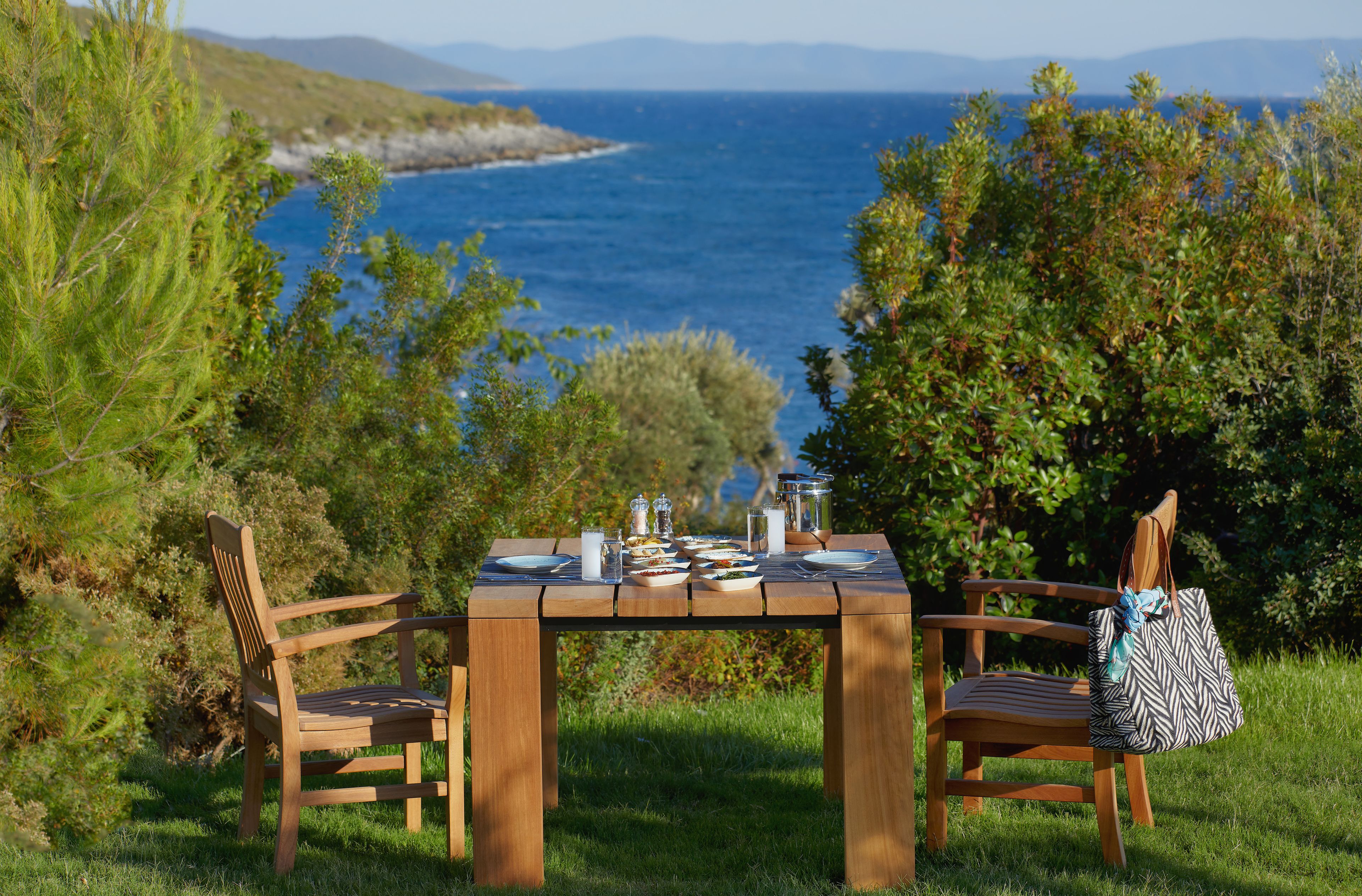 Une table en bois installée à l’extérieur, avec des chaises, un panier de pique-nique et une vue sur la mer.