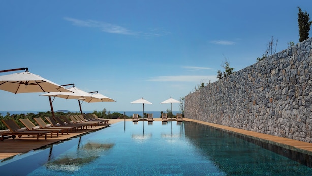 A pool with lounge chairs and umbrellas, surrounded by a stone wall and a clear view of the ocean. - Six Senses Kaplankaya (Milas)