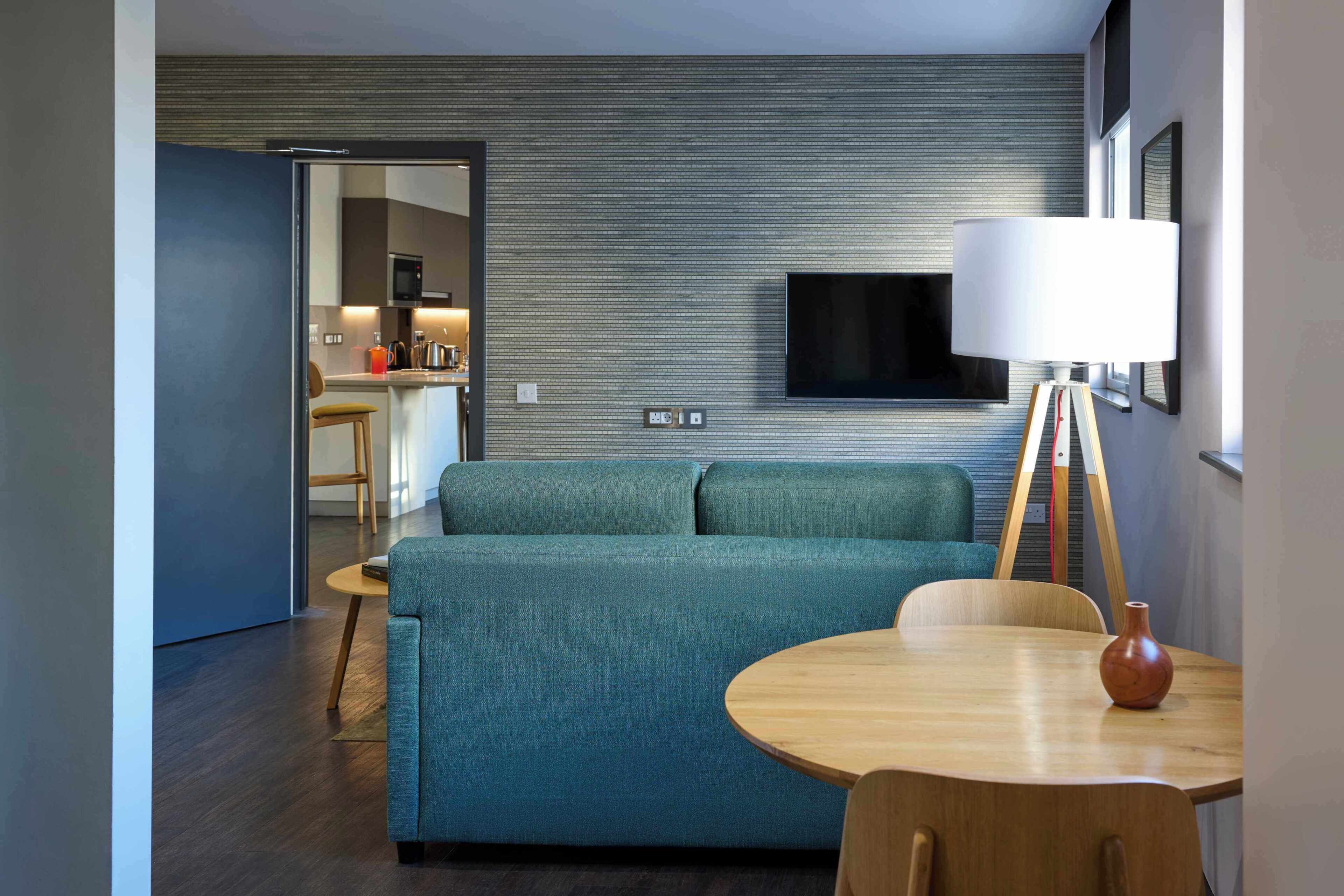 A modern living room with a sofa, a small round table, and a TV mounted on the wall.