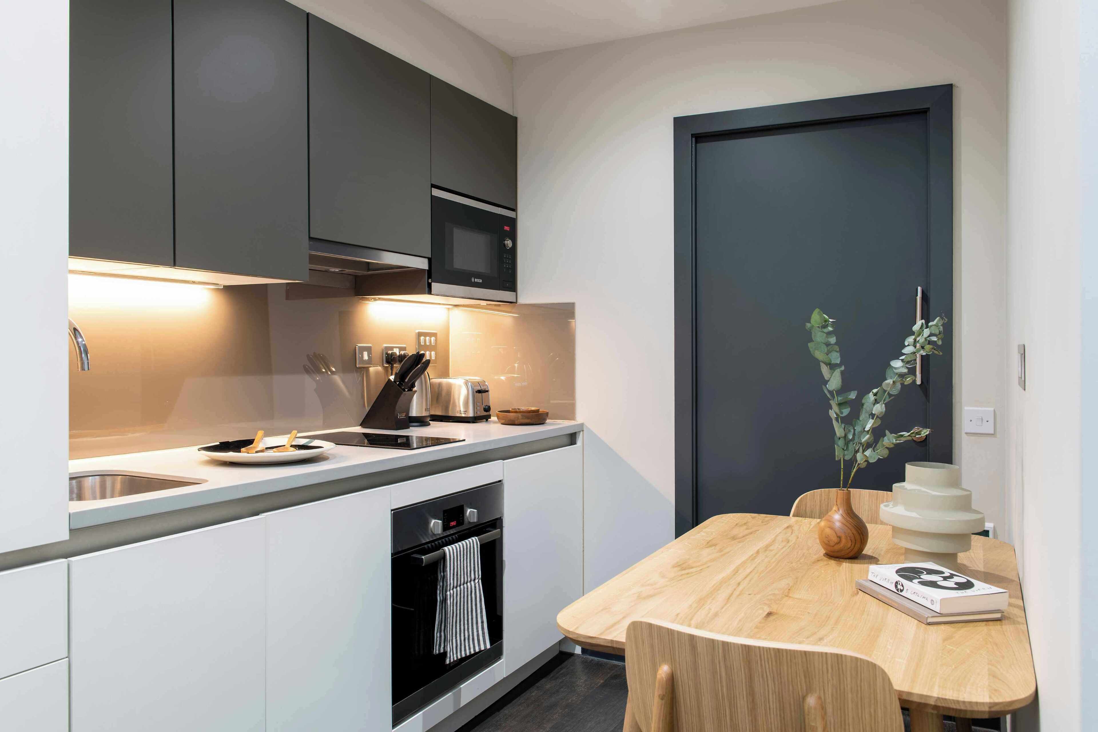 A modern kitchen with a built-in oven, microwave, and sink. There is a dining table with chairs and a vase with a plant.