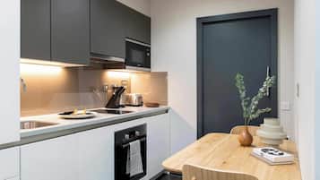 A modern kitchen with a built-in oven, microwave, and sink. There is a dining table with chairs and a vase with a plant.