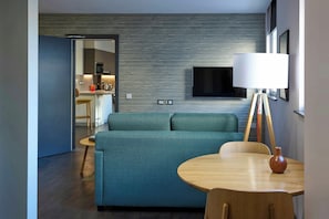A modern living room with a sofa, a small round table, and a TV mounted on the wall. - Cove Cannon Street (London)