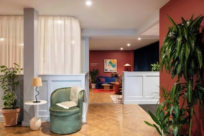 A modern hotel lobby with a green armchair, a potted plant, a floor lamp, and a reception desk. - Cove Cannon Street (London)
