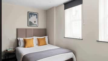 Ein Hotelzimmer mit Bett, Nachttisch, Wandbild und einem Fenster mit Jalousien.