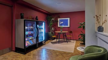 Une pièce avec un parquet en bois, un fauteuil vert, une petite table ronde, un réfrigérateur et une plante en pot.