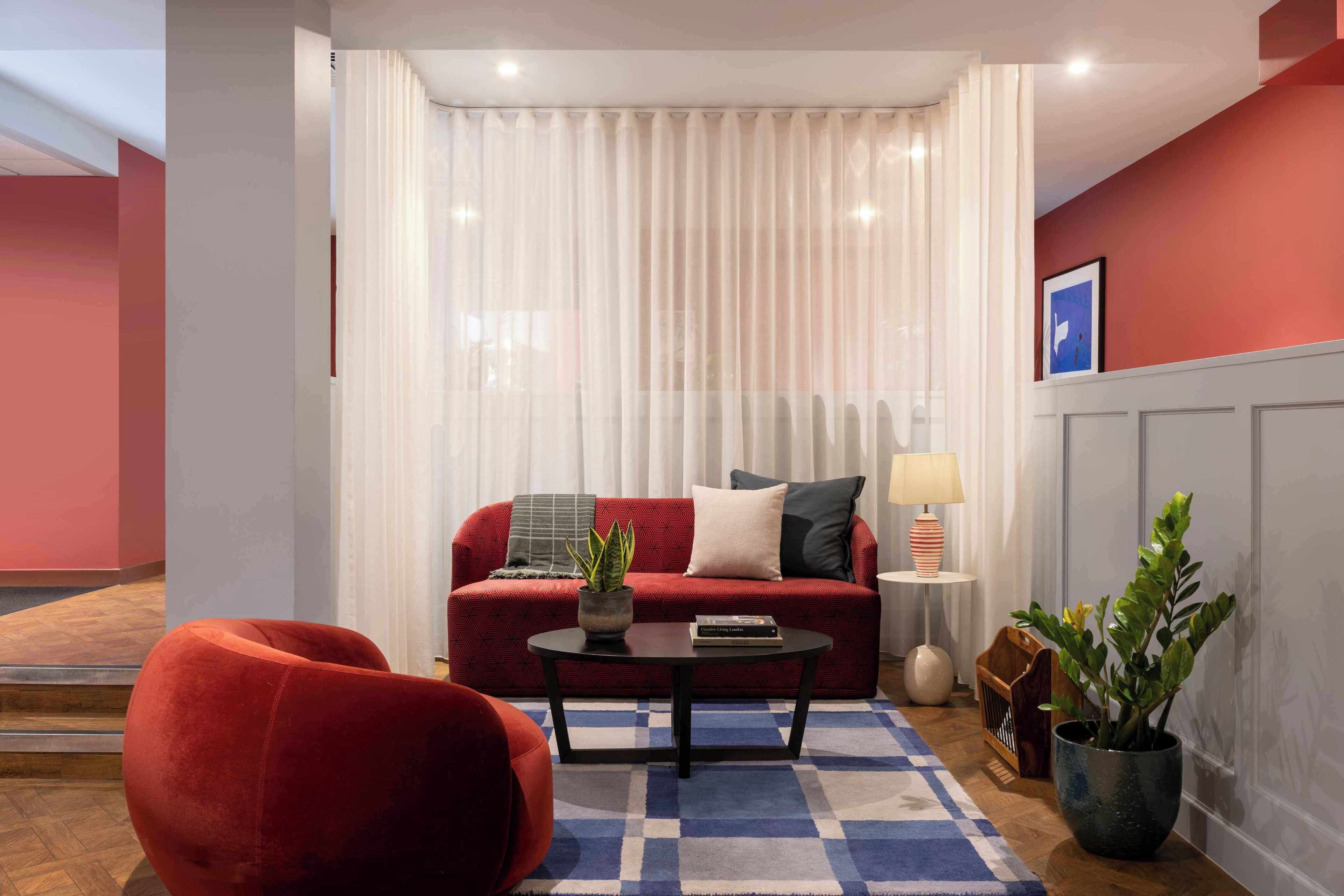 Un salon avec un canapé rouge, une table basse noire, un tapis bleu et blanc, une plante en pot et une lampe.