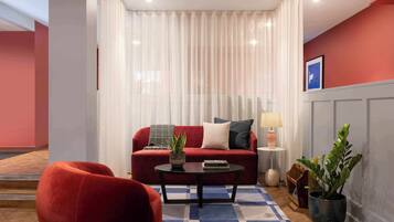 Un salon avec un canapé rouge, une table basse noire, un tapis bleu et blanc, une plante en pot et une lampe.