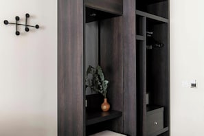 Une armoire en bois sombre, avec une plante posĂ©e sur lâĂ©tagĂšre intĂ©rieure, un crochet noir fixĂ© au mur et un petit tiroir.