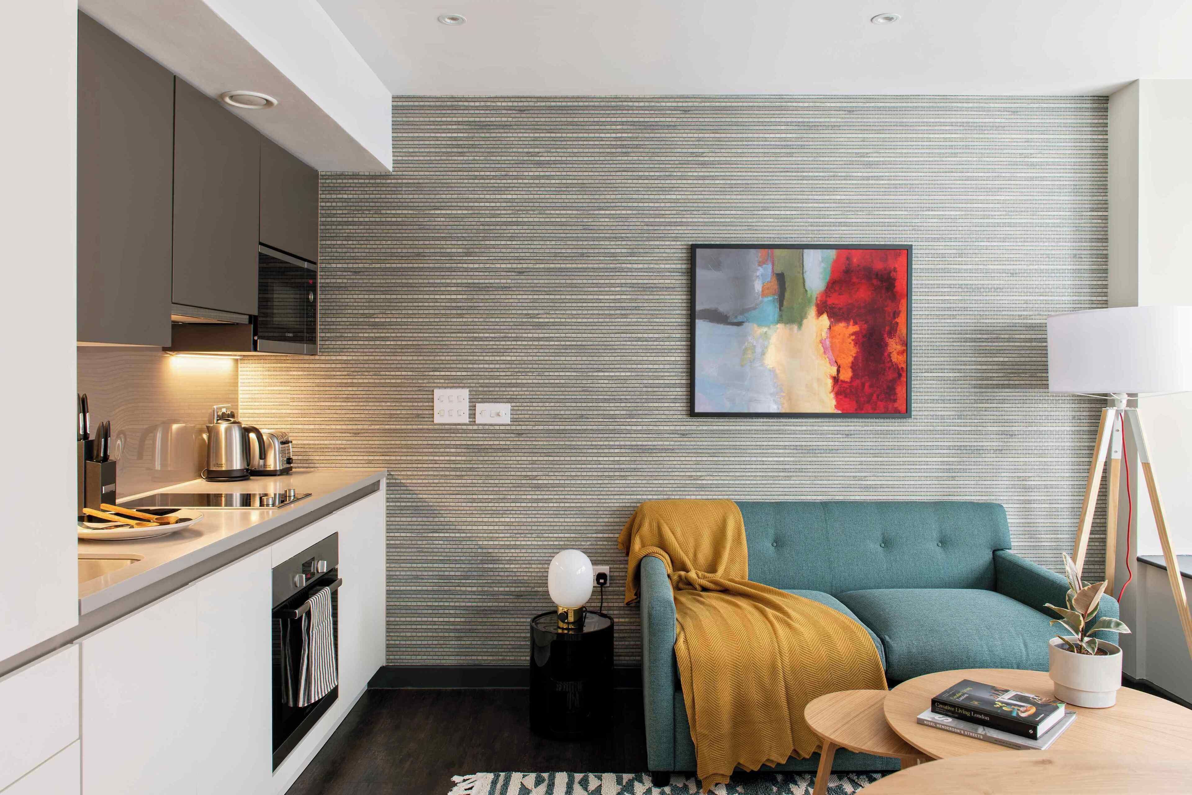 A modern kitchen with a built-in oven, a dining area with a table and chairs, a sofa, and a painting on the wall.