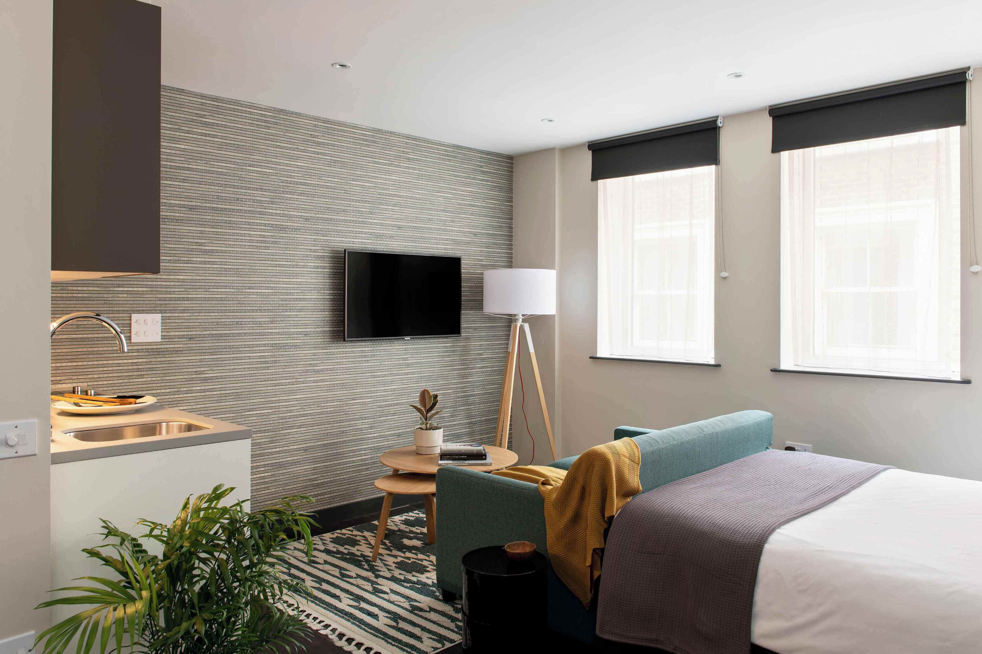 A modern hotel room with a bed, a sofa, a small table, a TV, and a window.