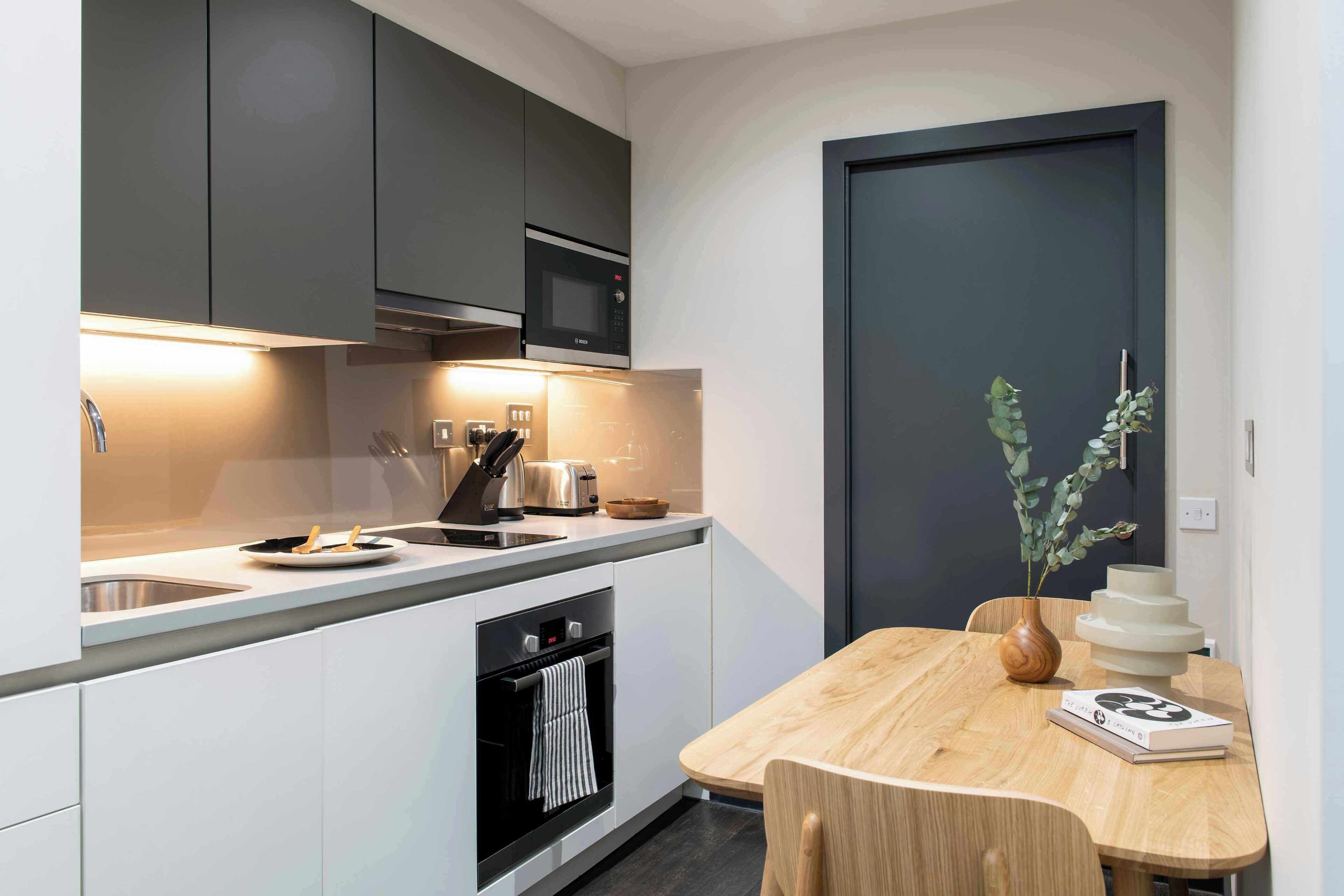 Una cocina moderna con microondas, tostadora y horno integrados. Hay una mesa de comedor con un florero y un libro.