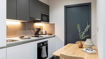 Una cocina moderna con microondas, tostadora y horno integrados. Hay una mesa de comedor con un florero y un libro.