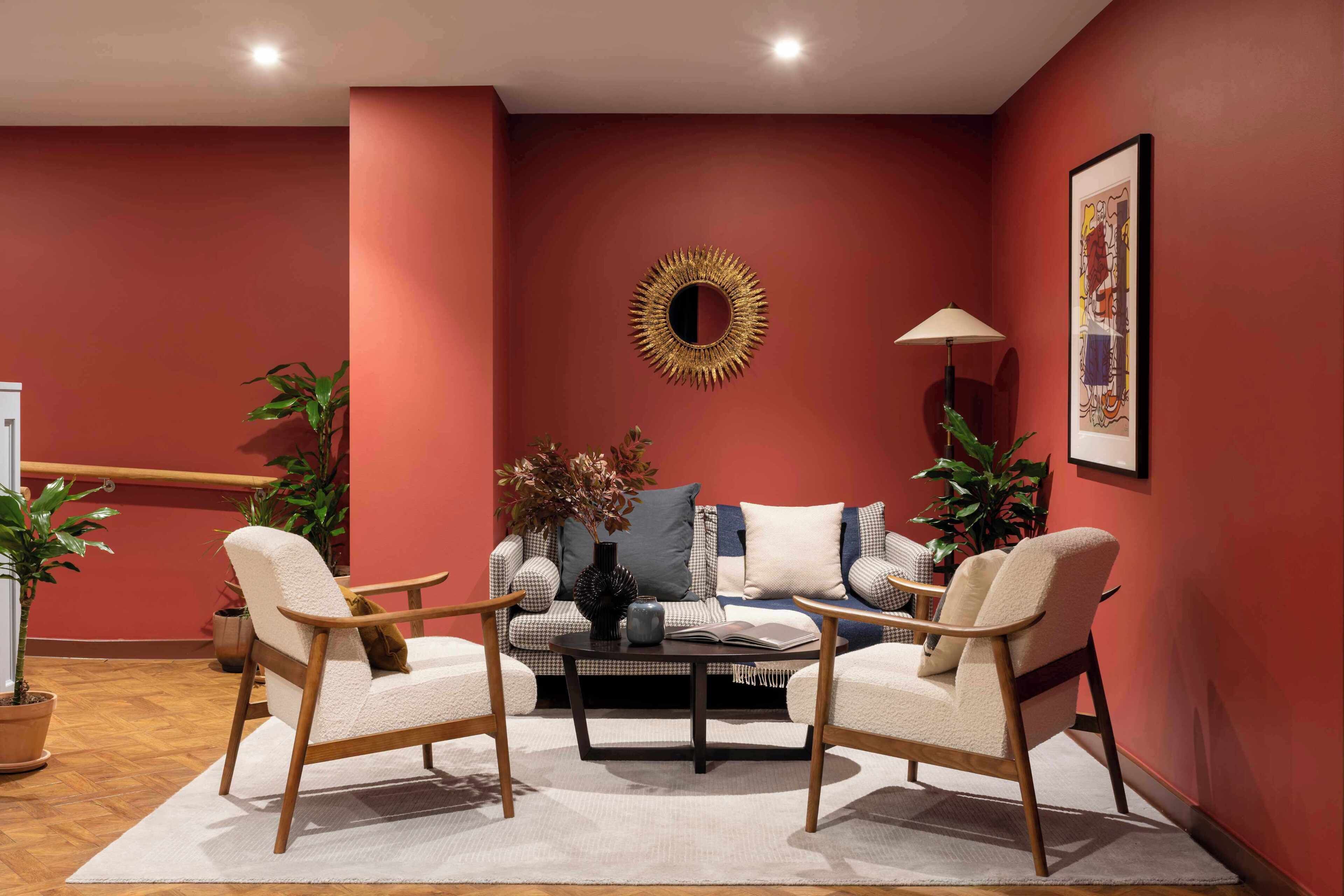 A living room with a red wall, a round mirror, a sofa, two armchairs, a coffee table, and a floor lamp.