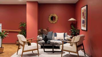 A living room with a red wall, a round mirror, a sofa, two armchairs, a coffee table, and a floor lamp.