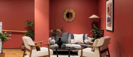 A living room with a red wall, a round mirror, a sofa, two armchairs, a coffee table, and a floor lamp.