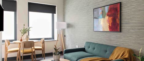 A modern living room with a green sofa, a round coffee table, a lamp, and a painting on the wall.