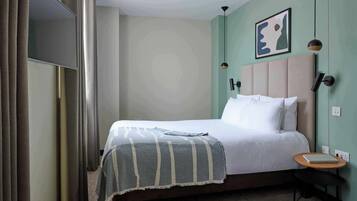 A neatly made bed with a striped blanket, a bedside table with a book, a wall-mounted light, and a framed picture.