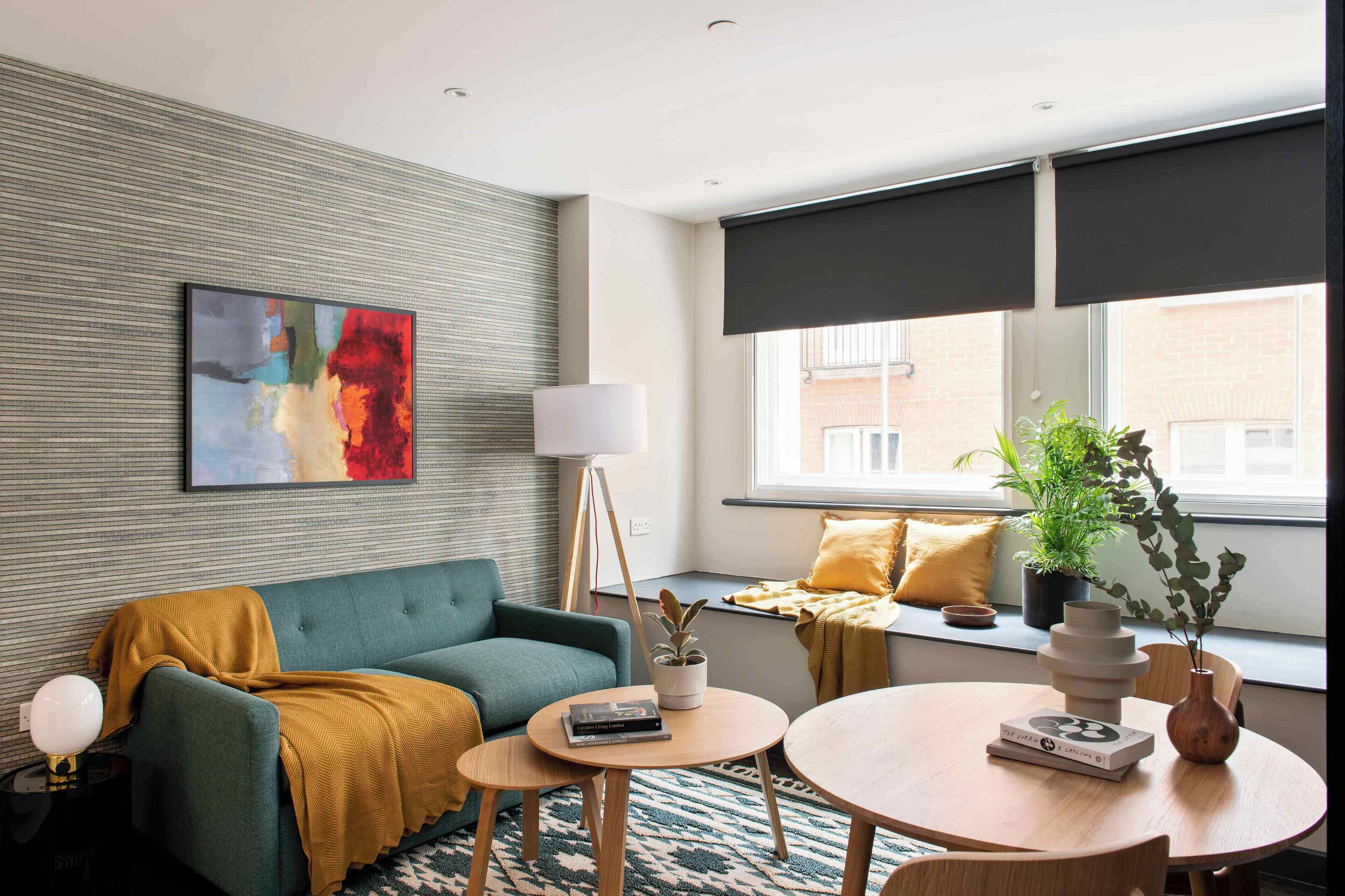 A modern living room with a sofa, a coffee table, a floor lamp, a window with blinds, and a painting on the wall.