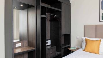 A hotel room with a large wardrobe, a bed with a white pillow, and a bedside table with a book.