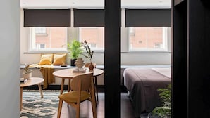 A modern hotel room with a large window, a bed, a small table with chairs, and a potted plant. - Cove Cannon Street (London)