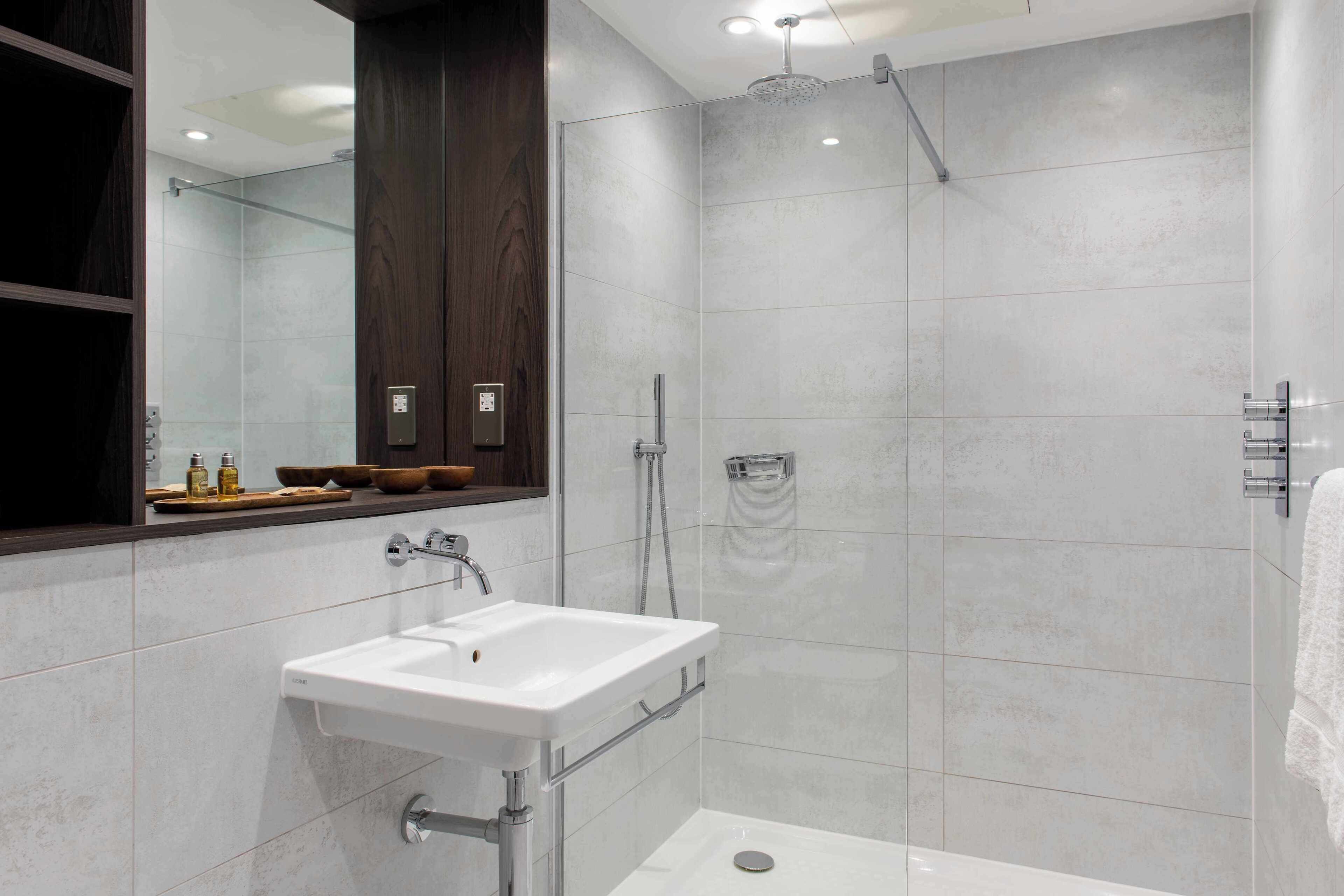 Un bagno moderno con un lavandino bianco, una cabina doccia in vetro e un mobile vanitario in legno con uno specchio.