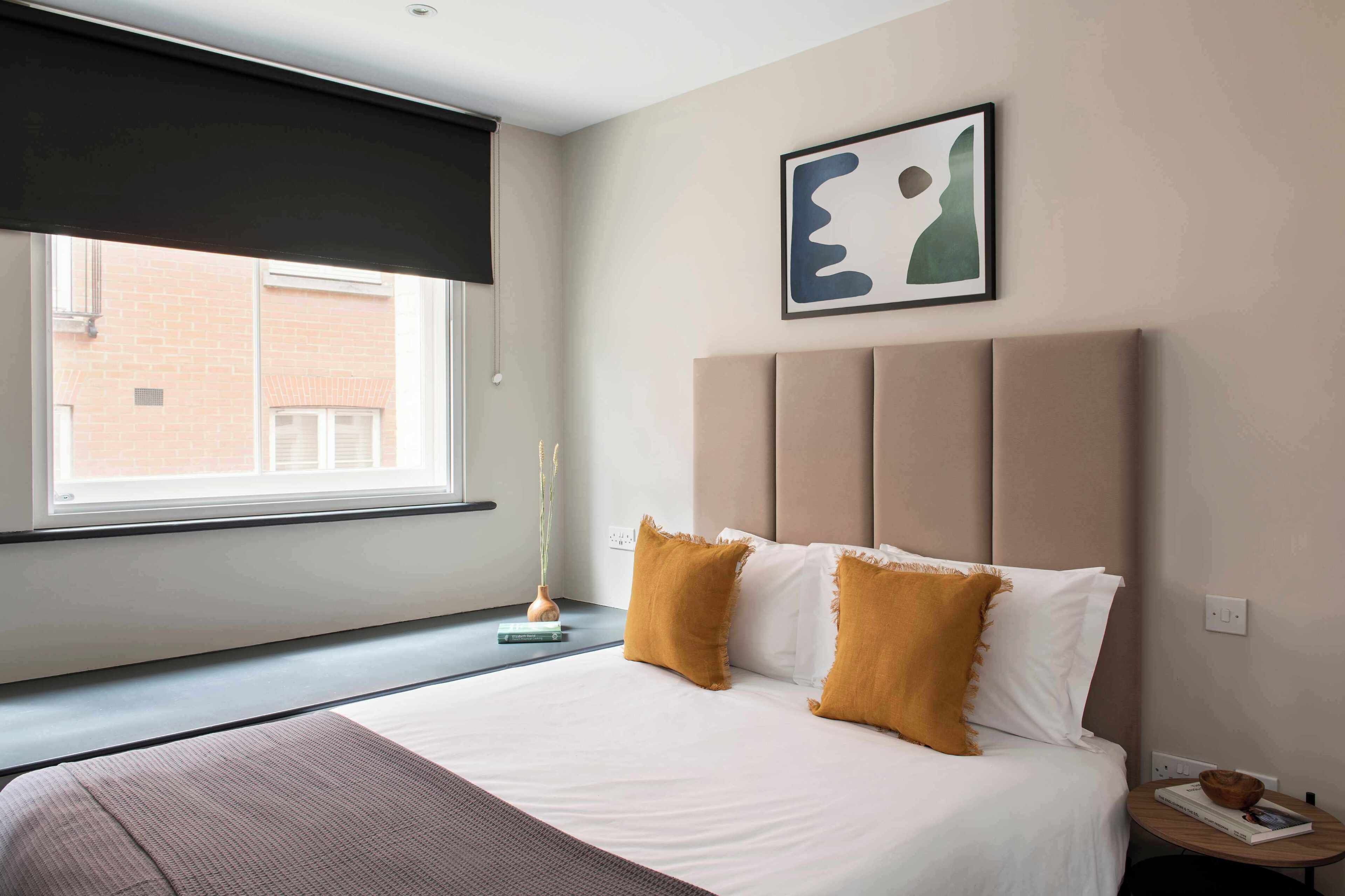 A bedroom with a bed, a window, a bedside table, and a wall-mounted artwork.