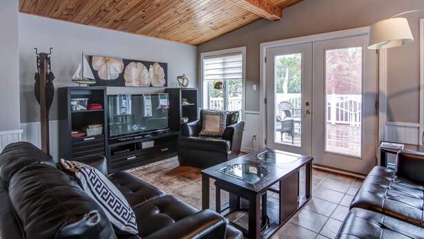 A living room with a wooden ceiling, a television, black leather sofas, and a glass coffee table. - La Maison du matelot (Alma)
