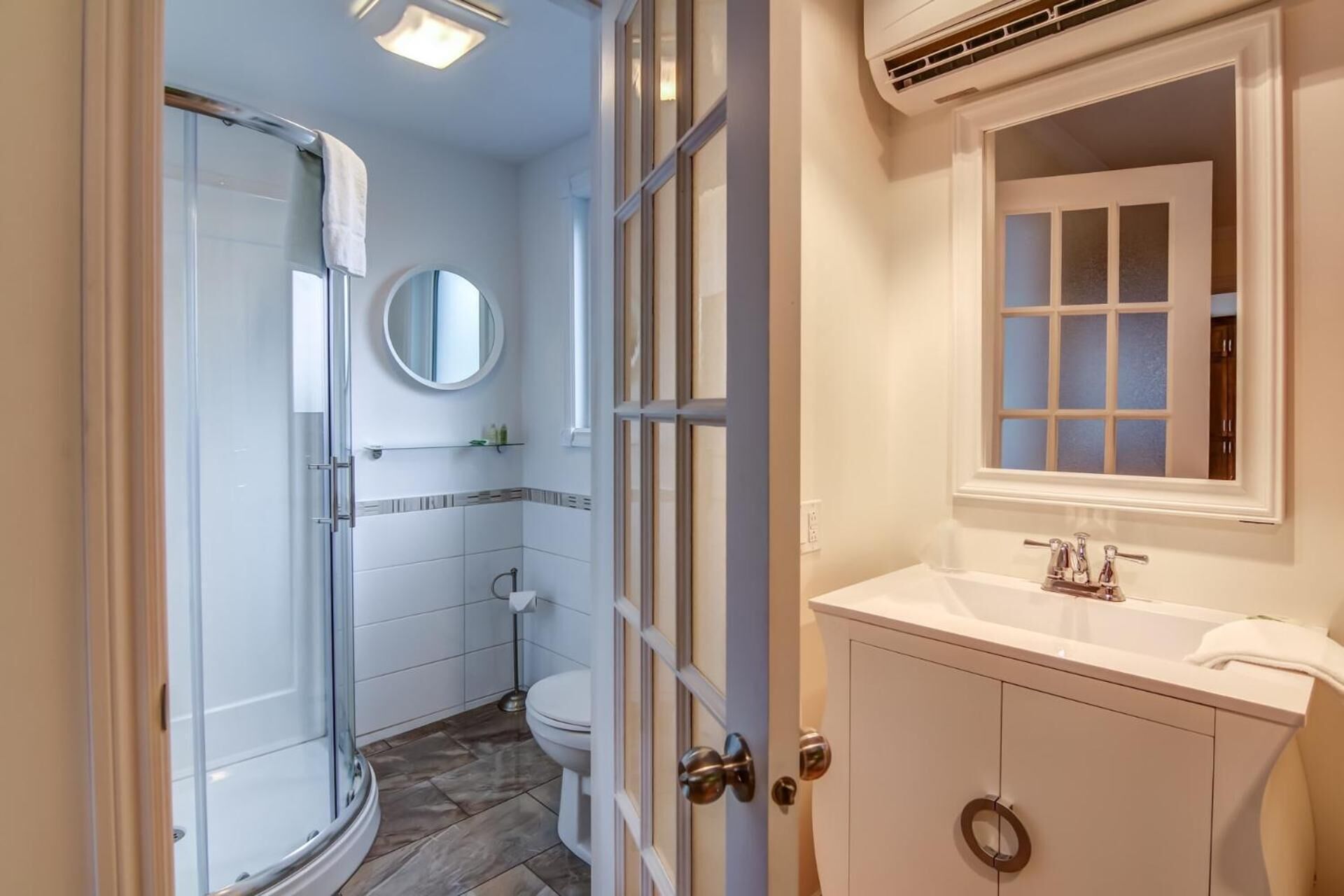 Une salle de bain avec une douche à parois de verre, des toilettes, un lavabo avec un miroir et une fenêtre avec des panneaux de verre dépoli.