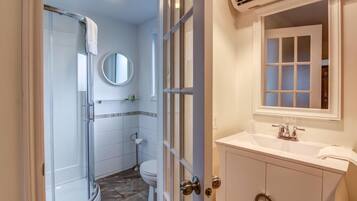 Une salle de bain avec une douche à parois de verre, des toilettes, un lavabo avec un miroir et une fenêtre avec des panneaux de verre dépoli.