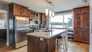 A modern kitchen with wooden cabinets, stainless steel appliances, and a large island with bar stools. - La Maison du matelot (Alma)