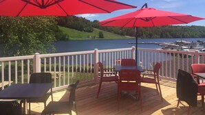 A deck with red umbrellas, a table, and chairs overlooking a lake. - La Maison du matelot (Alma)