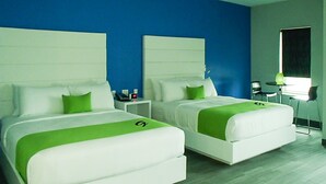 A hotel room with two beds, each with white bedding and green accents, a blue accent wall, and a small desk with a chair. - Garland Hotel (New Concord)