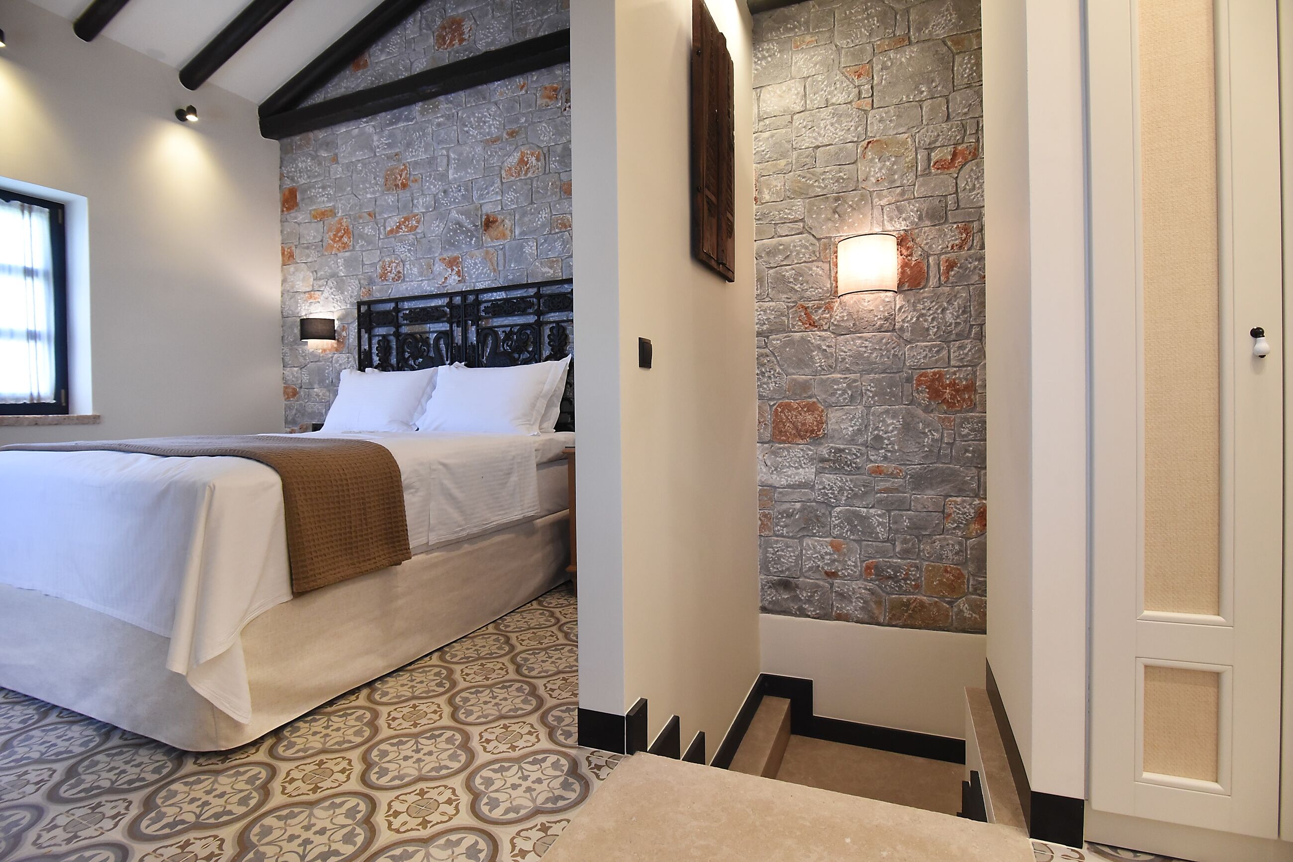 A bedroom with a bed, a stone wall, and a door.