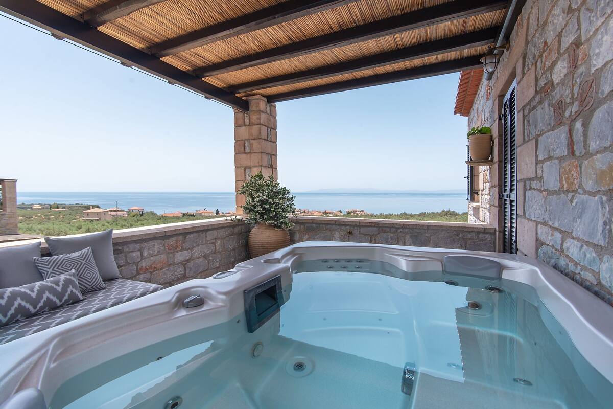 A hot tub with a stone wall and a view of the sea.