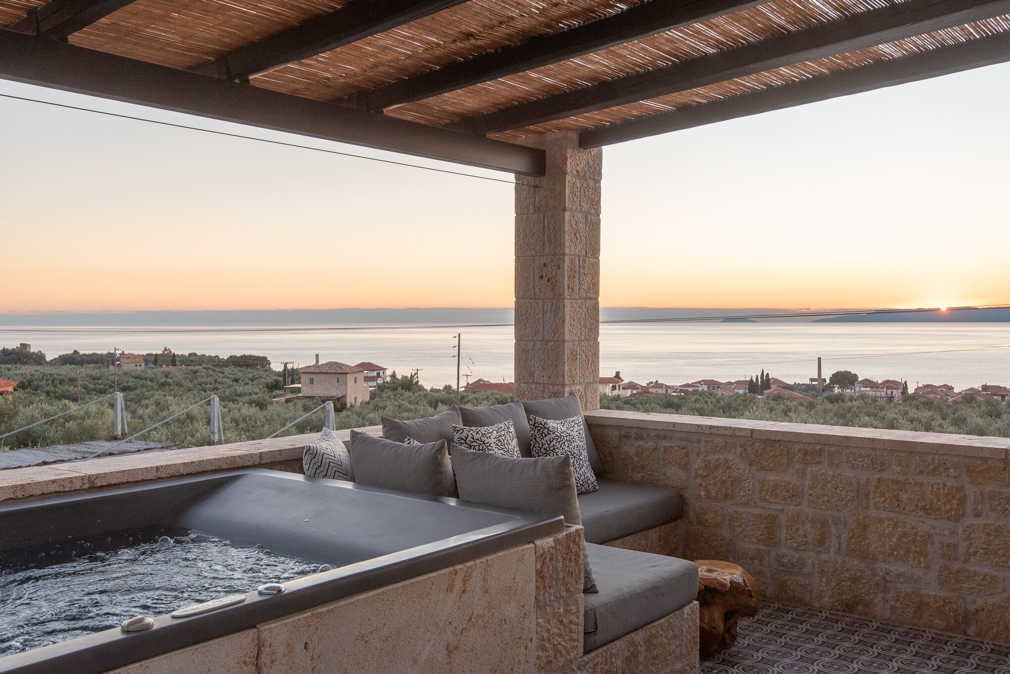 Une terrasse sur le toit avec un mur en pierre, un jacuzzi et une vue sur la mer.
