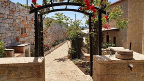 A stone pathway leading through a rustic gate with a wooden arch, flanked by stone walls and a building with a tiled roof. - Polismata - Private Residences (West Mani)