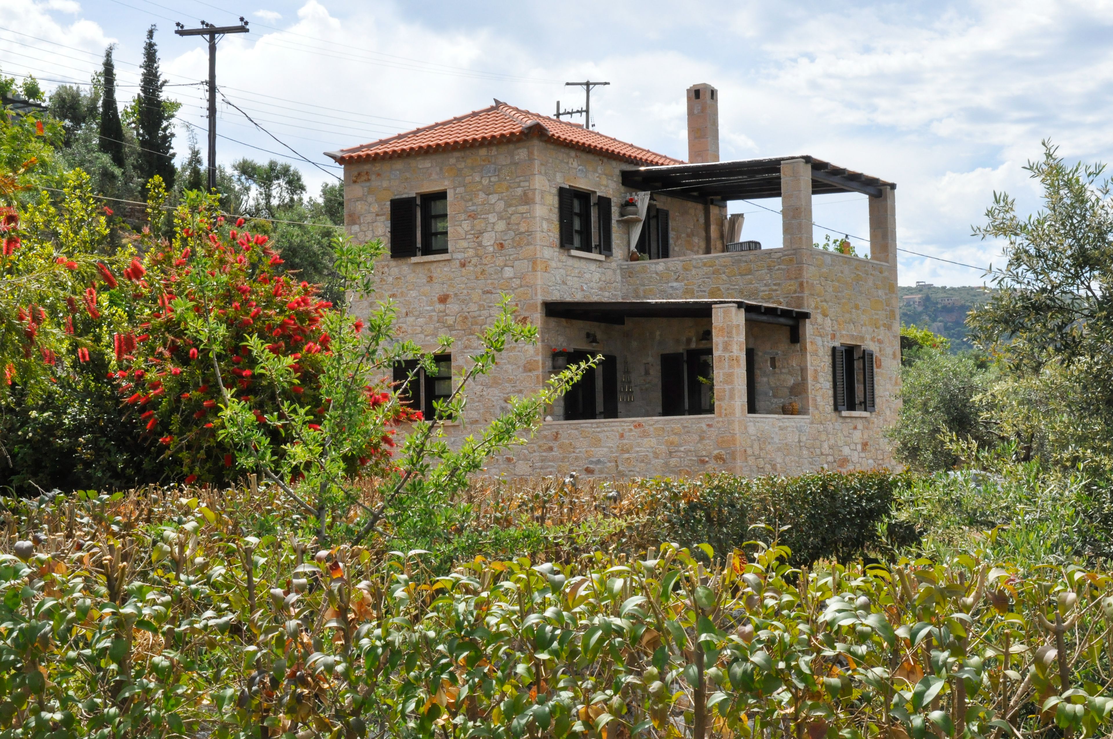 Un bâtiment en pierre avec un toit recouvert de tuiles rouges, dont la structure est partiellement constituée de poutres en bois apparentes et qui possède une cheminée.
