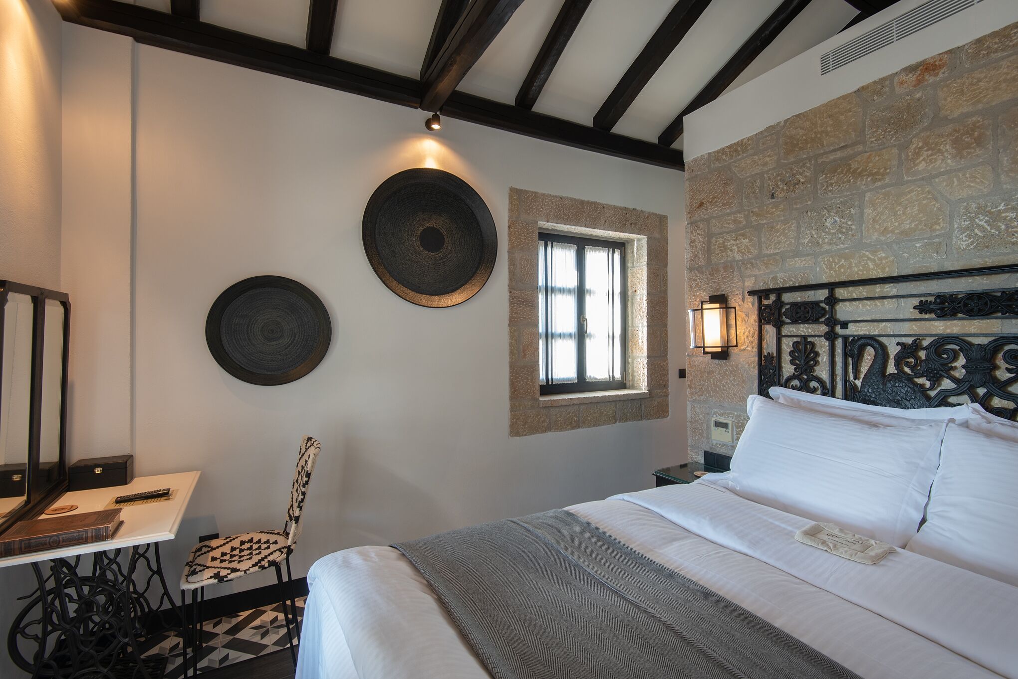A bedroom with a bed, a desk, and a chair. There is a window and a wall-mounted light fixture.