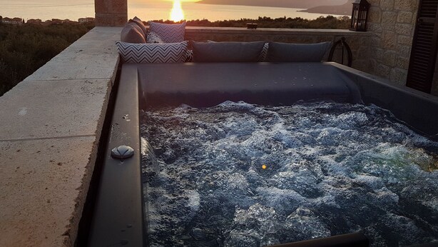 A hot tub with a view of the sunset over the sea, stone walls, and a stone pillar. - Polismata - Private Residences (West Mani)