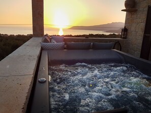 Un jacuzzi con vista al atardecer sobre el mar, paredes de piedra y un pilar de piedra.