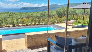 A pool with a view of the sea, a stone wall, and a swing chair. - Polismata - Private Residences (West Mani)