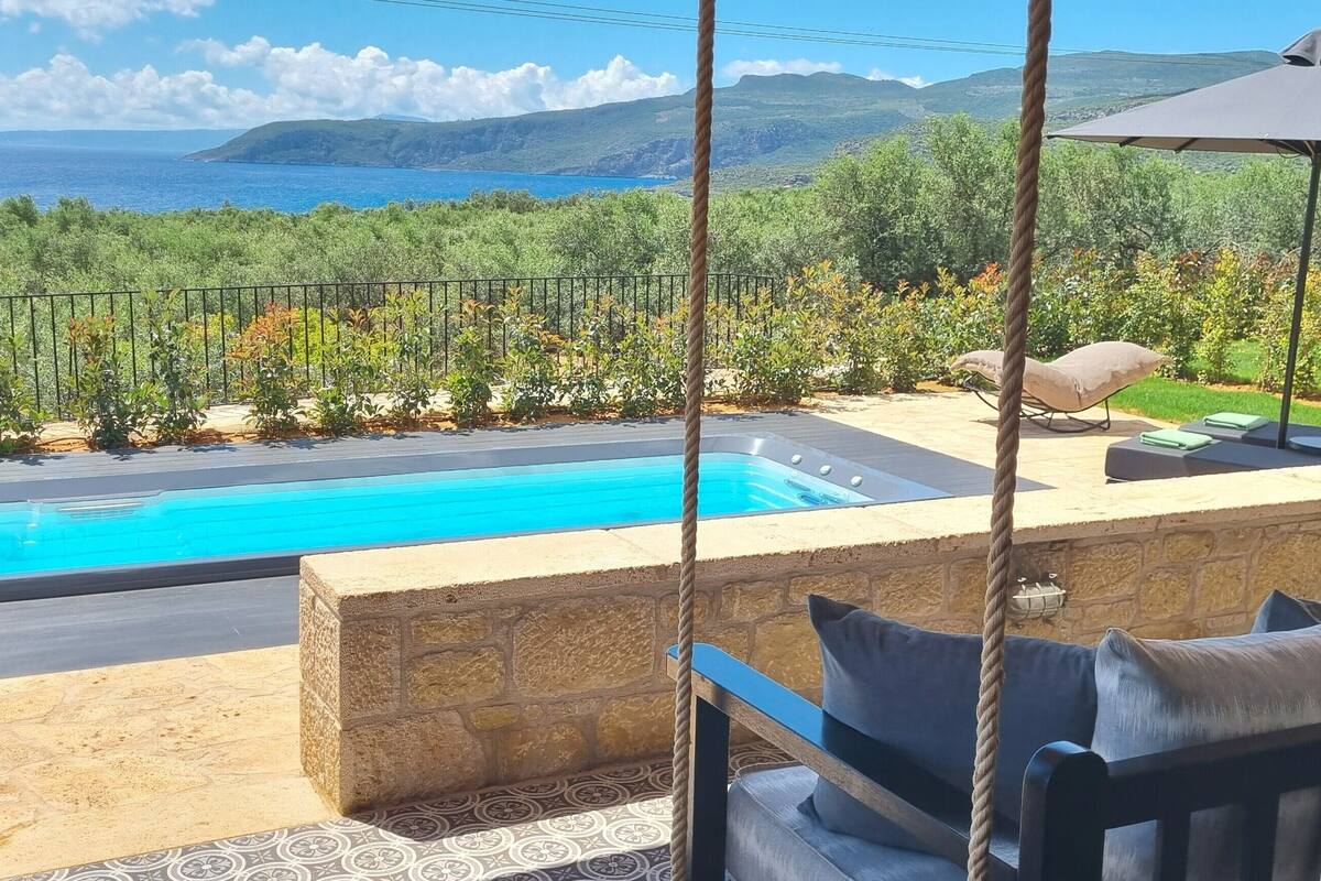 A pool with a view of the sea, a stone wall, and a swing chair.